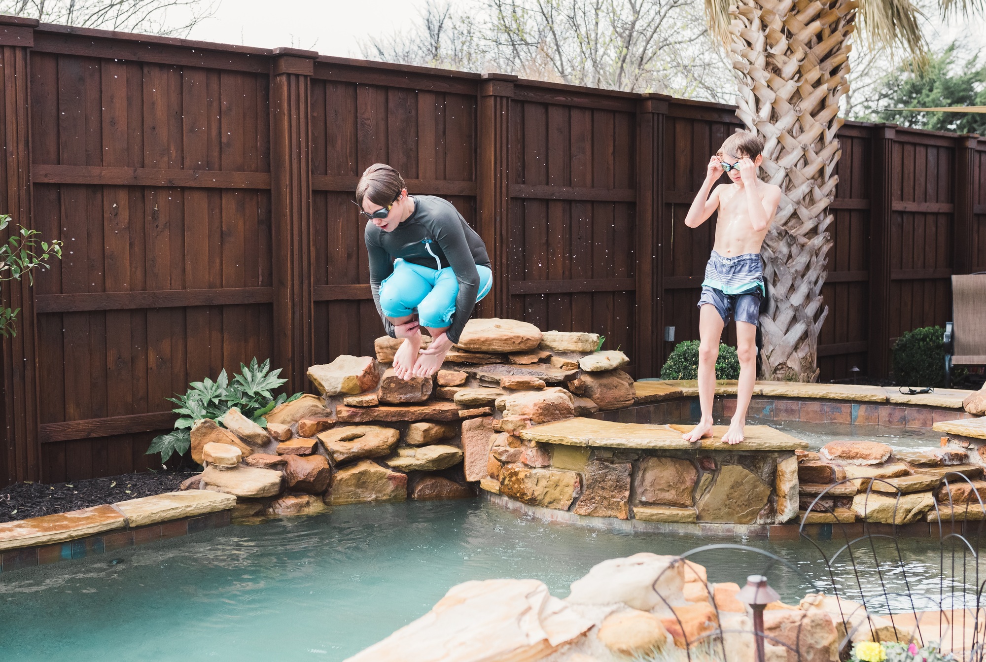 Two kids play in a nice backyard pool with a hot tub.